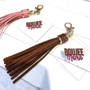 May include: Two clear acrylic keychains with gold key rings and brown and pink tassels. The keychains feature the text "BOUJEE MAMA" in pink letters.