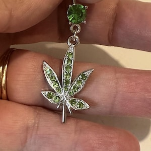 May include: A silver body piercing with a green crystal top and a green crystal marijuana leaf charm.