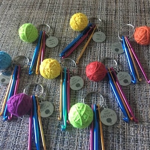 May include: A collection of colorful crochet-themed keychains. Each keychain features a small ball of yarn in various colors, a crochet hook, and a metal tag that reads "EAT SLEEP CROCHET". The hooks have a metallic finish.