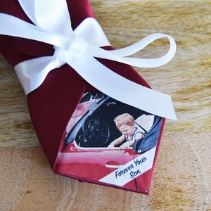 May include: A red tie with a white ribbon tied around it. The tie has a photo of a young boy in a car with the text "Forever Your Son" printed on it.