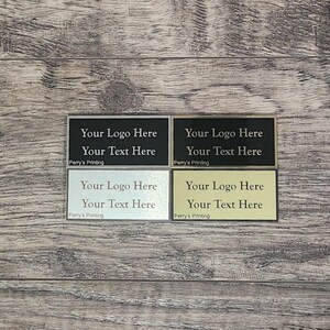 Display of four premium metal plate engraving color options for trophies: gold background with black text, silver background with black text, black background with silver text, and black background with gold text.