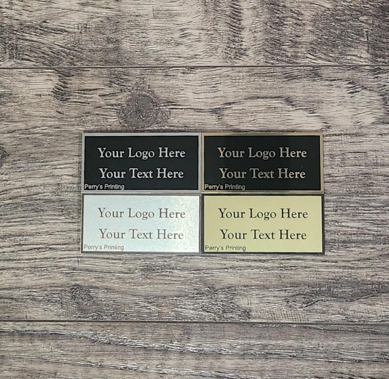 Display of four premium metal plate engraving color options for trophies: gold background with black text, silver background with black text, black background with silver text, and black background with gold text.