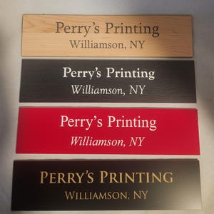 May include: Four rectangular signs with the text "Perry's Printing" and "Williamson, NY". The signs are in various colors: light wood, dark gray, red, and black. The text color varies from white to gold.