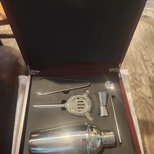 Premium cocktail shaker set presented in a luxurious rosewood box with black foam insert. The stainless steel barware set includes a shaker, jigger, strainer, mixing spoon, tongs, and stirrer. Perfect for home bartenders, mixology enthusiasts, and groomsmen gift sets.