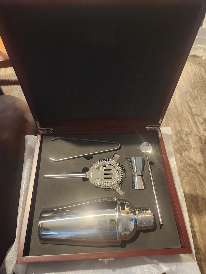 Premium cocktail shaker set presented in a luxurious rosewood box with black foam insert. The stainless steel barware set includes a shaker, jigger, strainer, mixing spoon, tongs, and stirrer. Perfect for home bartenders, mixology enthusiasts, and groomsmen gift sets.
