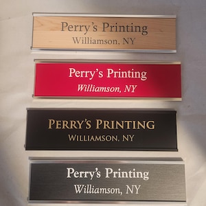 May include: Four nameplates with the text "Perry's Printing, Williamson, NY." The nameplates have different colored backgrounds: wood grain, red, black, and brushed metal. The text is in different colors.