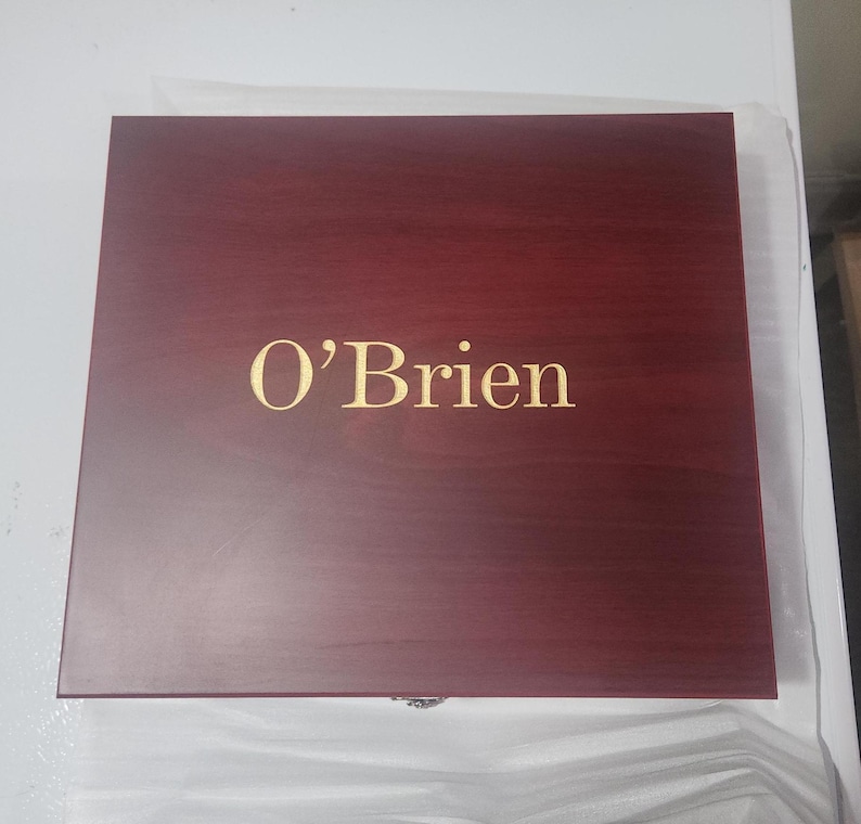 May include: A rectangular, wooden box with a dark red finish. The name "O'Brien" is displayed in gold lettering on the top of the box. The box is closed and appears to be new.