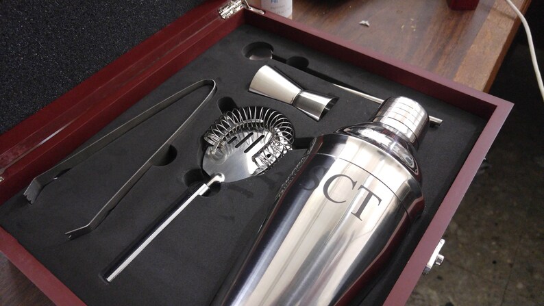 Personalized martini cocktail set in a rosewood finish gift box featuring stainless steel bar tools including a shaker engraved with initials 'CT', strainer, jigger, stirrer, and ice tongs. The tools are securely nestled in custom-cut foam for a premium presentation. Ideal for weddings, groomsmen gifts, Father’s Day, anniversaries, or home bar essentials. A stylish and functional gift for cocktail enthusiasts or mixology lovers.