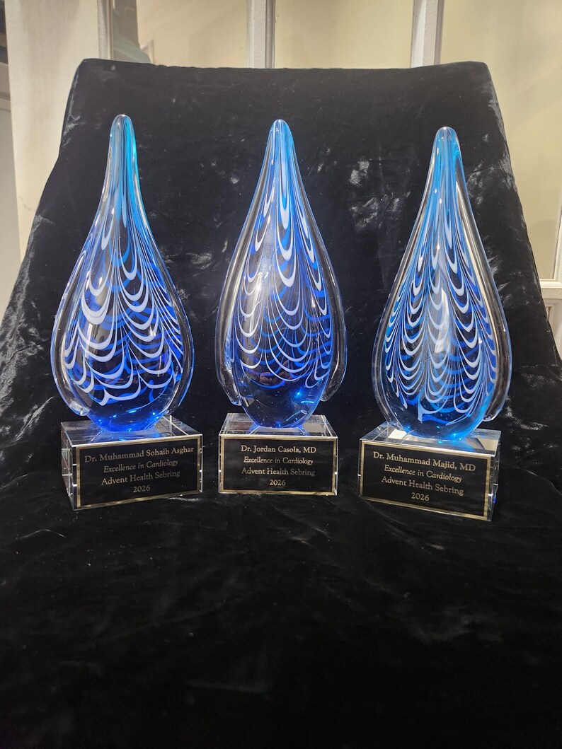 May include: Three teardrop-shaped glass awards featuring blue and white swirling patterns. Each award sits on a clear rectangular base with a black plaque engraved with the text: Dr. Muhammad Sohaib Asghar, Dr. Jordan Casola, MD, and Dr. Muhammad Majid, MD.