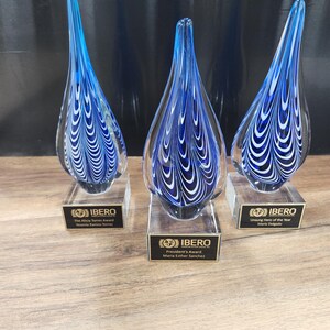 Set of 3 elegant hand-blown glass teardrop awards featuring a striking blue and white swirl design. Mounted on clear bases with custom engraved nameplates, these artistic trophies are ideal for corporate recognition, employee appreciation, or special achievement awards. Perfect for events honoring excellence, leadership, or service. Unique artisan craftsmanship adds a sophisticated touch to any ceremony or display.
