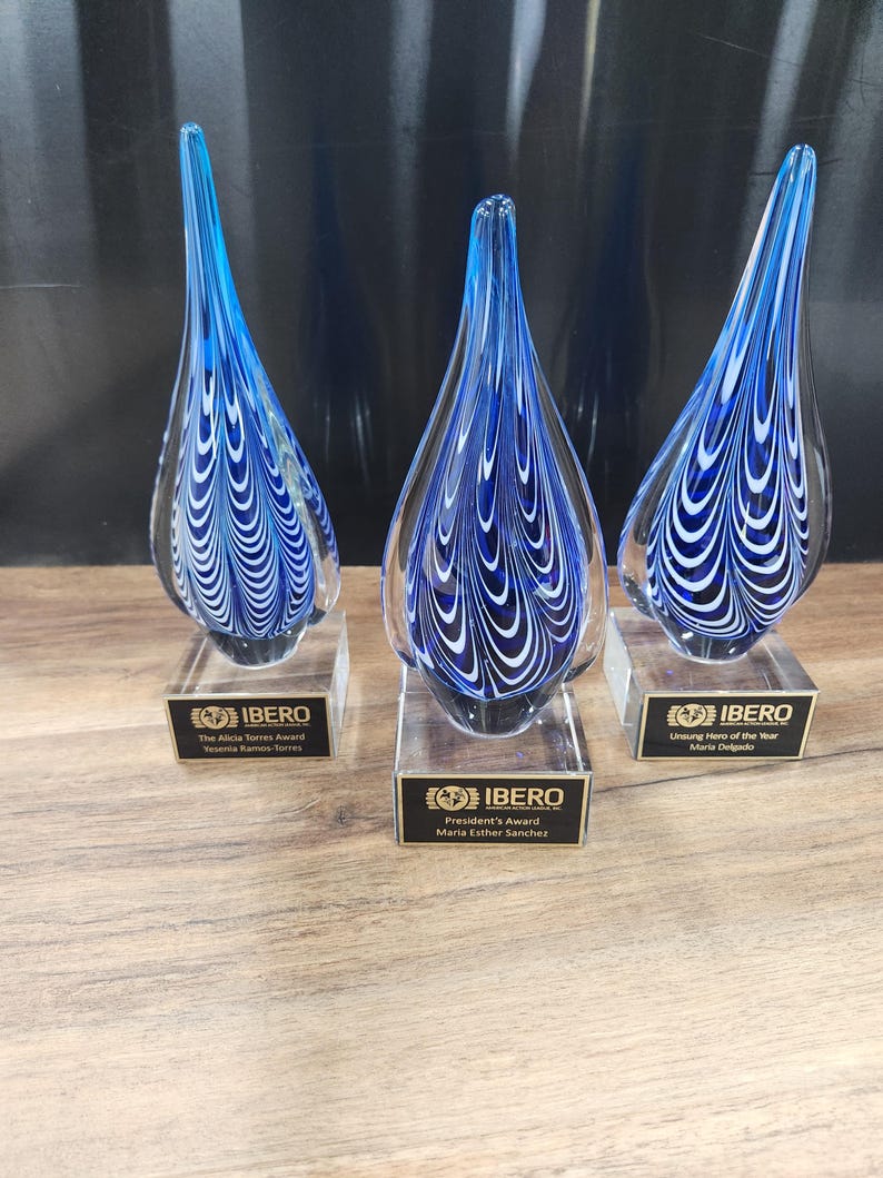 Set of 3 elegant hand-blown glass teardrop awards featuring a striking blue and white swirl design. Mounted on clear bases with custom engraved nameplates, these artistic trophies are ideal for corporate recognition, employee appreciation, or special achievement awards. Perfect for events honoring excellence, leadership, or service. Unique artisan craftsmanship adds a sophisticated touch to any ceremony or display.