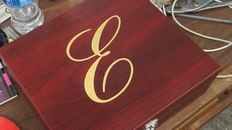 Close-up of a personalized rosewood finish gift box featuring an engraved and gold color-filled script initial 'E'. The elegant monogram design is centered on the box lid, making it ideal for a custom cocktail gift set, barware set, or special occasion present. This engraved wood box offers a luxurious presentation and is perfect for weddings, groomsmen, Father's Day, anniversaries, or corporate gifting.