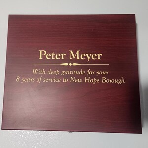 May include: A rectangular, dark red wooden plaque with gold lettering. The text reads "Peter Meyer" above the inscription "With deep gratitude for your 8 years of service to New Hope Borough."