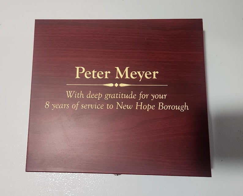 May include: A rectangular, dark red wooden plaque with gold lettering. The text reads "Peter Meyer" above the inscription "With deep gratitude for your 8 years of service to New Hope Borough."
