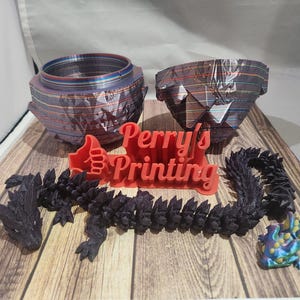 May include: A collection of 3D-printed items, including two geometric planters with a striped pattern, a black articulated dragon, a small colorful frog, and a red sign that says "Perry's Printing".