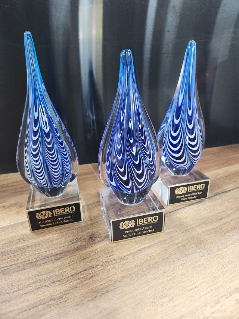 Set of three artisan glass teardrop awards featuring stunning blue and white swirl patterns, mounted on clear rectangular bases with custom engraved nameplates. Ideal for corporate recognition, appreciation ceremonies, or employee achievement awards. Elegant design makes each piece a unique and memorable gift or display item for honoring excellence and dedication. Perfect for office décor or award showcases.