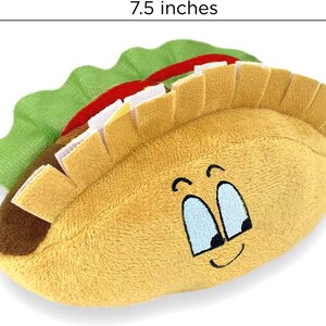May include: A plush toy shaped like a taco with a smiling face. The taco is 7.5 inches long and has a brown shell, green lettuce, and a red and white filling.