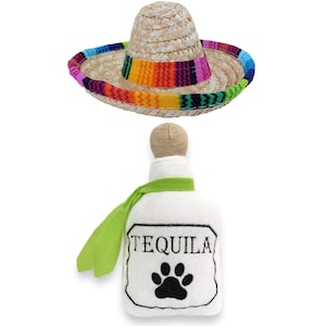 Op de afbeelding: Een witte pluche tequilafles met een groene sjaal en een zwarte pootprint. De fles heeft het woord "Tequila" geborduurd. Een strooien sombrero met een kleurrijke band is ook inbegrepen.