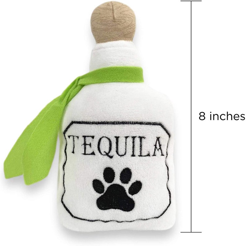 Op de afbeelding: Wit pluche hondenspeelgoed in de vorm van een tequilafles met een groen lint en een zwarte pootprint. De fles is 20 cm hoog en heeft het woord "TEQUILA" op het etiket.