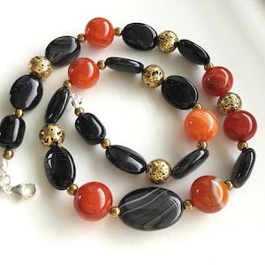 May include: A necklace made with black and orange agate beads and gold spacers. The necklace has a silver clasp.