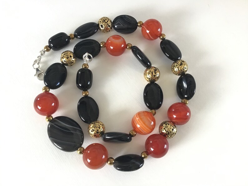 May include: A necklace made with black and orange agate beads and gold-toned spacers. The necklace is approximately 18 inches long.