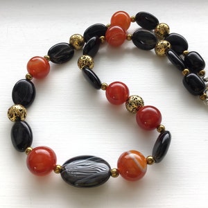 May include: A necklace made with black and orange agate beads and gold spacers.