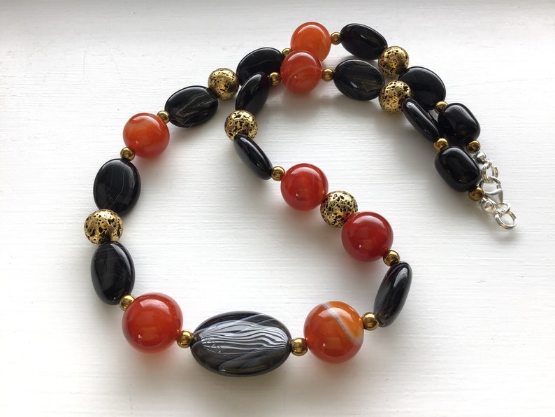 May include: A necklace made with black and orange agate beads and gold spacers.