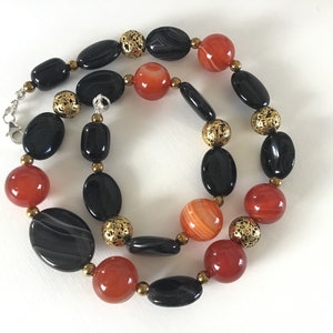 May include: A necklace made with black and orange agate beads and gold-toned spacers. The necklace is approximately 18 inches long.