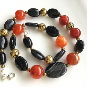 May include: A necklace made with black and orange agate beads and gold spacer beads. The necklace has a silver clasp.