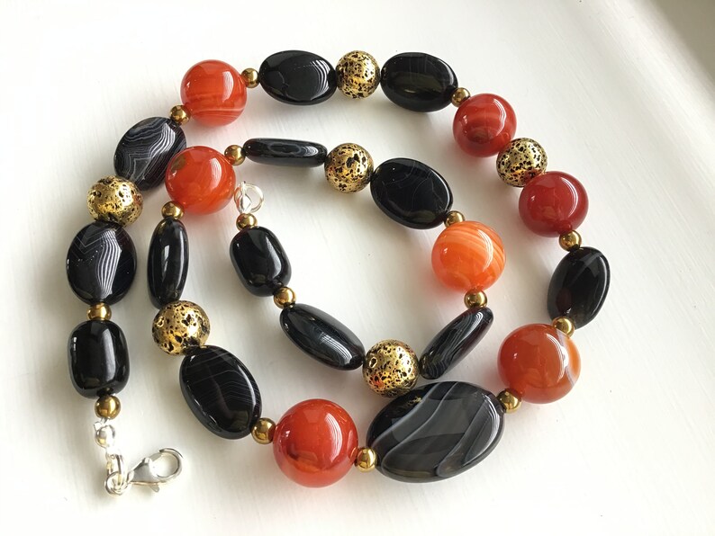 May include: A necklace made with black and orange agate beads and gold spacer beads. The necklace has a silver clasp.