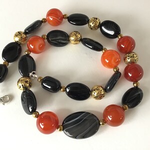 May include: A necklace made with black and orange agate beads and gold spacer beads. The necklace has a silver clasp.