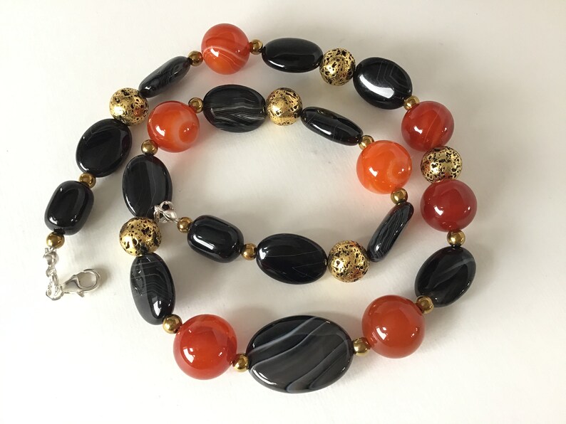 May include: A necklace made with black and orange agate beads and gold spacer beads. The necklace has a silver clasp.