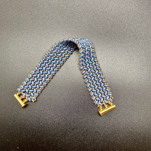 May include: A blue and gold beaded bracelet with a woven pattern. The bracelet has gold clasps on each end.