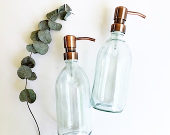May include: Two clear glass bottles with copper pump tops. The bottles are empty and have a frosted look.