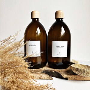 May include: Two amber glass bottles with cork tops and white labels. The bottle on the left says "bath salts" and the bottle on the right says "bubble bath".