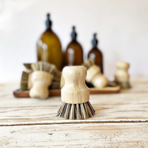 May include: A set of four small, round, wooden brushes with natural bristles. The brushes are made of bamboo and have a light brown colour. The brushes are sitting on a wooden surface.
