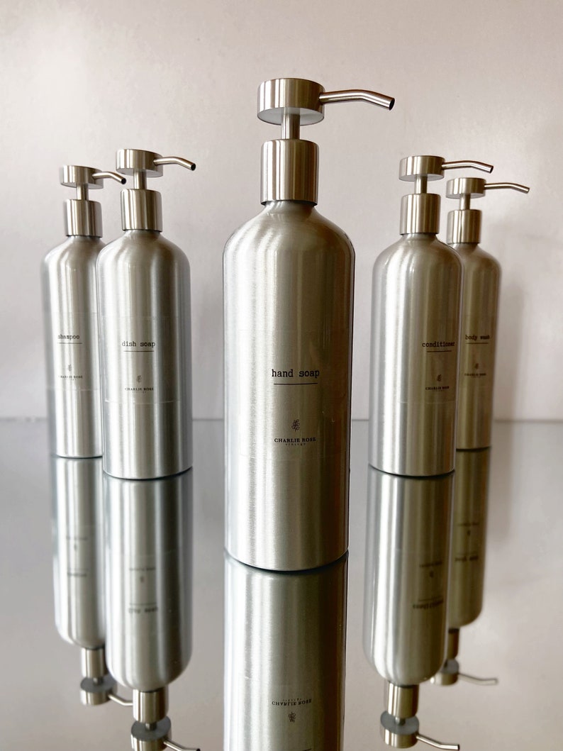 May include: Five silver pump bottles with black labels. The labels read "shampoo", "dish soap", "hand soap", "conditioner", and "body wash".