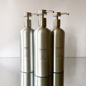 May include: Three silver pump bottles with labels reading "shampoo", "body wash", and "conditioner". Each bottle has the text "Charlie Rose" and a small floral design.