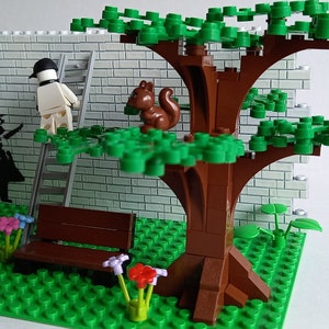 May include: A Lego model of a park scene with a brick wall, a tree, a bench, and a figure painting a mural. The mural depicts a girl holding a balloon. A squirrel sits on a branch of the tree.