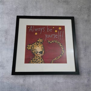Könnte beinhalten: Gerahmtes Kunstwerk mit einem Cartoon-Leoparden mit einem tan- und schwarz gefleckten Fell. Der Leopard ist vor einem burgunderroten Hintergrund mit den Worten "Always be yourself!" in weißer Schrift gesetzt. Das Kunstwerk ist in einem schwarzen Rahmen gerahmt.