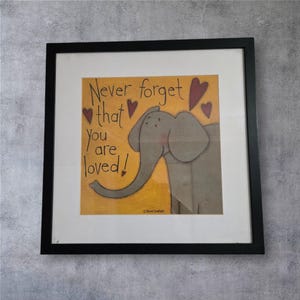 Könnte beinhalten: Gerahmtes Kunstwerk mit einer Elefantenillustration und dem Text "Never forget that you are loved!" in Schwarz. Der Hintergrund ist gelb mit roten Herzen, der Rahmen ist schwarz.