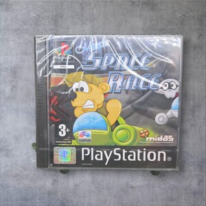 Könnte beinhalten: Versiegeltes PlayStation-Spielcase für "Midas Space Race". Das Cover zeigt einen Cartoon-Bären in einem grünen Fahrzeug, mit dem Spieltitel in Weiß und Blau. Das Case ist in Klarsichtfolie verpackt.
