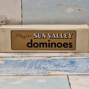 Peut inclure: Une boîte blanche avec une inscription dorée qui dit "Player's SUN VALLEY dominoes".