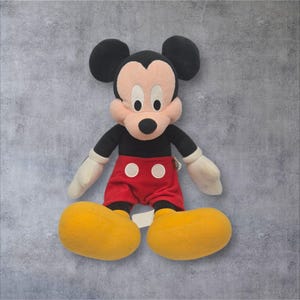 K&ouml;nnte beinhalten: Eine Mickey-Maus-Stoffpuppe mit schwarzem Kopf und gro&szlig;en runden Ohren, pfirsichfarbenem Gesicht, schwarzer Nase und wei&szlig;en Augen. Die Puppe tr&auml;gt einen schwarzen Oberk&ouml;rper, wei&szlig;e Handschuhe, eine rote Hose mit zwei wei&szlig;en runden Kn&ouml;pfen und gro&szlig;e gelbe Schuhe.