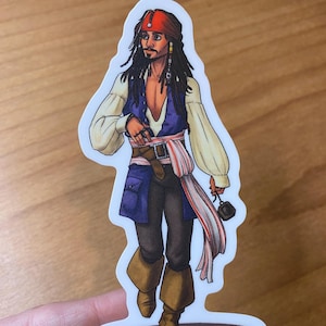 Peut inclure: Une illustration de bande dessinée de Captain Jack Sparrow de la franchise de films Pirates des Caraïbes. Il porte un bandana rouge, un gilet bleu, une chemise blanche, un pantalon marron et des bottes marron. Il tient un petit objet noir dans sa main droite.