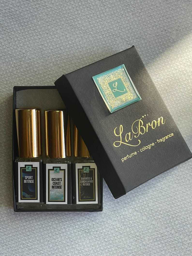 May include: A black box with a gold logo that says "La Bron perfume - cologne - fragrance". The box contains three small glass bottles with gold caps. The bottles are labeled "Sport Intense", "Ocean's Coast Intense", and "Oakmoss & Sandalwood Intense".