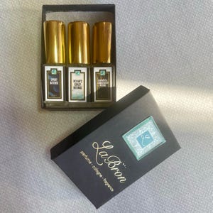 May include: A black box with the text "La Bron perfume cologne - fragrance" on the front. The box contains three small glass bottles of perfume with gold caps. The bottles are labeled "Sport Intense", "Ocean's Coast Intense", and "Darkness & Sandalwood Intense".
