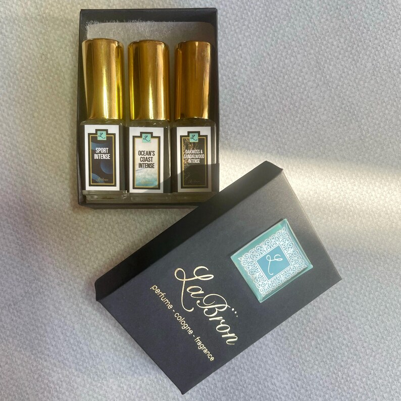 May include: A black box with the text "La Bron perfume cologne - fragrance" on the front. The box contains three small glass bottles of perfume with gold caps. The bottles are labeled "Sport Intense", "Ocean's Coast Intense", and "Darkness & Sandalwood Intense".