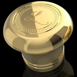 May include: Gold bottle stopper with a decorative top featuring a stylised letter L.