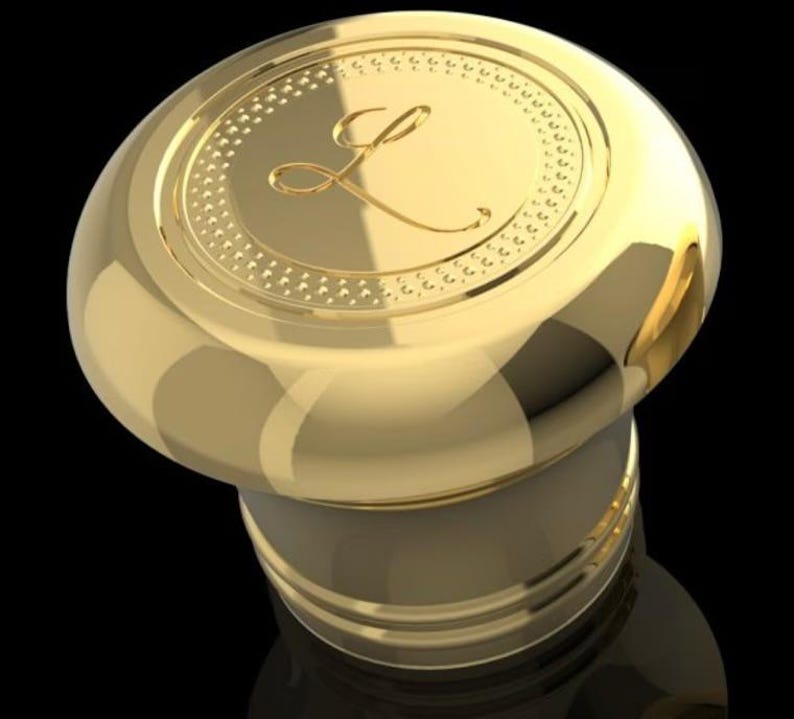 May include: Gold bottle stopper with a decorative top featuring a stylised letter L.